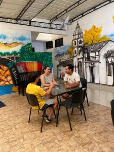 un grupo de personas sentadas en una mesa frente a un mural en Aparta Hotel El Cacique Upar en Valledupar