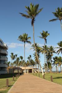 a boardwalk leading to the beach with palm trees at Lindo Apartamento pé na areia com serviço de limpeza in Lauro de Freitas