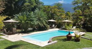 a swimming pool in a yard with chairs and umbrellas at Pousada Florence in Ilhabela