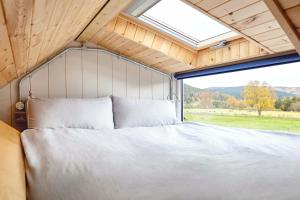 uma cama num quarto com uma grande janela em Unique tiny house with wood fired roll top bath in heart of the Cairngorms em Ballater