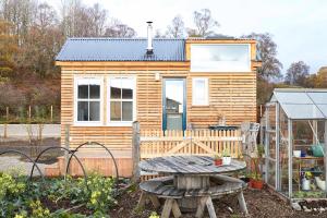 a tiny house with a picnic table and a greenhouse at Aileen - Unique tiny house with wood fired roll top bath in heart of the Cairngorms in Ballater