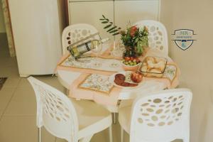 ein Tisch mit weißen Stühlen und ein Teller mit Essen drauf in der Unterkunft Recanto da Musica Maragogi l Condomínio com 4 casas in Maragogi