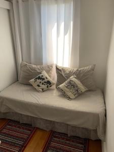 Cette chambre comprend un lit avec des oreillers et une fenêtre. dans l'établissement Quartos Vila Augusta/Guarulhos, à Guarulhos