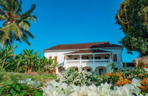 a white house with a palm tree and flowers at The Manor House by Sansi in Zanzibar City