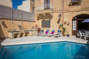 a swimming pool in front of a building with chairs at Tal Lilly Xaghra in Xagħra