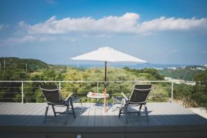 une table, deux chaises et un parasol sur une terrasse dans l'établissement Motobu Terrace, à Motobu