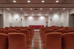 an empty lecture hall with orange chairs and a stage at Villa Nazareth Fermo in Fermo