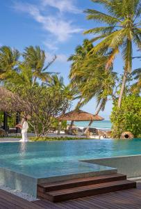 un homme debout à côté d'une piscine bordée de palmiers dans l'établissement Naladhu Private Island Maldives - Special Offer On Transfer Rates For Summer 2024, à Atoll Malé Sud