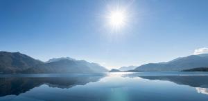 a sun shining over a body of water with mountains at Hotel Du Lac Menaggio in Menaggio