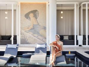 
a woman sitting at a table in front of a large window at Hotel Chadstone Melbourne, MGallery by Sofitel in Chadstone
