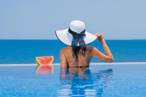 a woman in the water with a hat and a slice of watermelon at Nerea SeaFront Villa, a Pristine Retreat, By ThinkVilla in Akrotiri