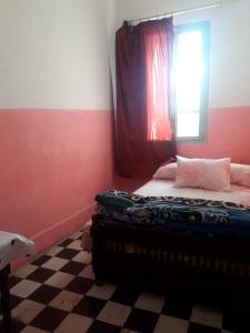 a bedroom with a bed with a window and a checkered floor at Hôtel Glacier in Fez
