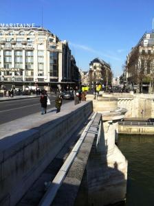 a group of people walking on a sidewalk next to a river at Into Paris - Louvre Apartment in Paris