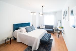 a white bedroom with a bed and a blue chair at Expoholidays - General Tamayo PARKING gratis in Almería