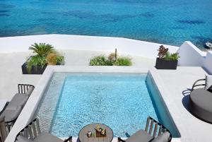uma piscina de beiral infinito num pátio com cadeiras e uma mesa em Aeonic Suites and Spa em Míconos