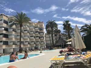 a resort swimming pool with chaise lounges and palm trees at BAMBOO CHIC APARTMENT PLAYA DEL INGLES in Playa del Ingles