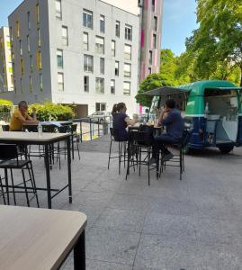 un groupe de personnes assises à des tables dans un patio dans l'établissement Just For Sleep-daily stay 8pm to 10am Apres votre arrivee dans le batiment d'entree, contact I'hote via le message ici de reservation pour l'enregistrement I'entree dans la propriete sans I'approbation est interdite-Resevation d'un tiers est inacceptable-, à Bobigny