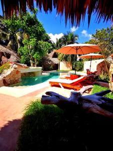 un patio trasero con piscina, sombrilla y sillas en Hotel Circulo Bacalar en Bacalar