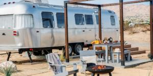 an rv parked in the desert with a table and chairs at AutoCamp Joshua Tree in Joshua Tree