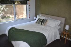 a white bed with a green blanket and a window at CALYPSO RETREAT - Modern townhouse - Ocean views in Portarlington