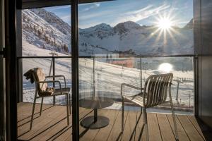 two chairs and a glass table on a balcony with mountains at Hôtel VoulezVous by Les Etincelles in Tignes