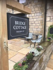 ein Schild für ein Café mit zwei Stühlen und Blumen in der Unterkunft Bridge Cottage in Cowling