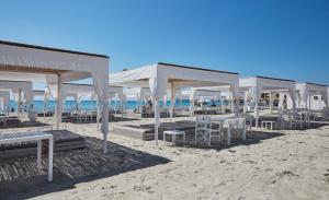 einen Strand mit Tischen, Stühlen und weißen Sonnenschirmen in der Unterkunft VOI Tanka Village in Villasimius