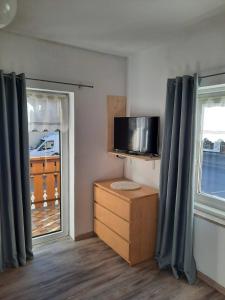 Pokój z telewizorem, komodą i dwoma oknami w obiekcie Appartamento Casa Montagna Lory w mieście Pozza di Fassa