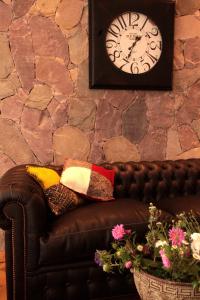 un sofá de cuero marrón con almohadas y un reloj en una pared de piedra. en Hotel Boutique Balcón de la Plaza en Salta