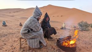 two women sitting next to a fire in the desert at Nomadic Desert Camp Tours in Merzouga