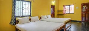 Radhabai Hotel في أرامبول: سريرين في غرفة بجدران صفراء ونوافذ