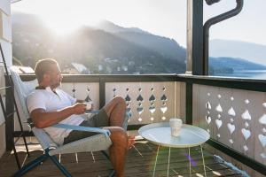 un hombre sentado en una silla en un balcón con una mesa en SEEGLÜCK Hotel Forelle Superior, en Millstatt