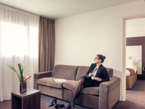 une femme assise sur un canapé dans une chambre d'hôtel dans l'établissement Mercure Paris Porte d'Orleans, à Montrouge