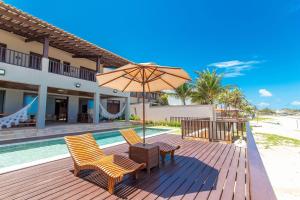 um deque com cadeiras e um guarda-sol junto a uma piscina em Casa de Luxo na Beira Mar de Porto Mirim/RN em Jacumã