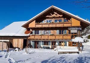 duży drewniany dom z balkonem w śniegu w obiekcie Landhaus Wanger w mieście Pfronten