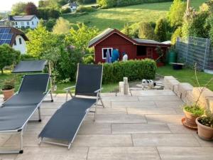eine Terrasse mit 2 Stühlen, einem Tisch und einem Hund in der Unterkunft Ferienhaus Sommerhaus-Sauerland in Hachen