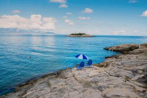 two chairs with an umbrella sitting on a rocky shore at Kokkinos Studios in Skinária