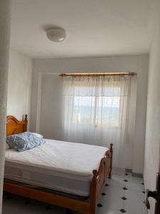 1 dormitorio con 1 cama con ventana y colcha blanca en Rodafam, en Playa de Miramar