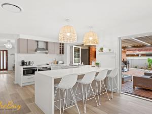a kitchen with white cabinets and a bar with stools at Waves on Whitesands in Fingal Bay