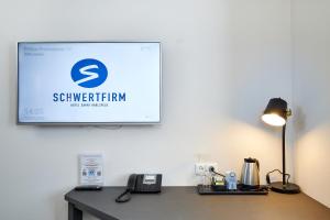 a television on a wall with a desk with a phone at Hotel Schwertfirm in Karlsfeld