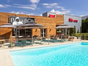 a pool with chairs and umbrellas in front of a restaurant at Ibis Roanne Le Coteau Hotel Restaurant in Le Coteau