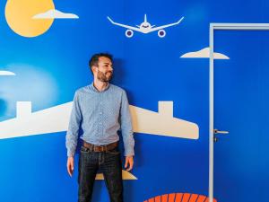 a man standing in front of a blue wall with an airplane at ibis Styles Nice Aéroport Arenas in Nice