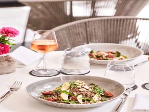 a table with a bowl of salad and a glass of wine at Athens Capital Center Hotel - MGallery Collection in Athens