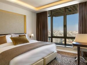 a bedroom with a large bed and a desk and window at Mövenpick Hotel Amman in Amman