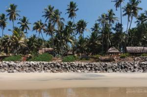 a rocky beach with palm trees in the background at Sukriti beach Resort in Varkala