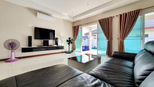 ein Wohnzimmer mit einem Ledersofa und einem TV in der Unterkunft Ban Sabai Sabai Pool Villa in Cha-am