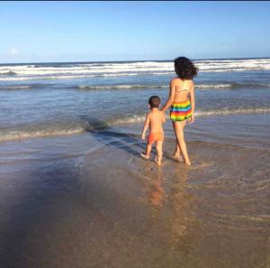 a woman and a child walking on the beach at Apê de Mainha in Ilhéus