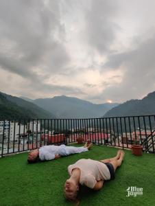 Dois homens deitados na relva numa varanda. em Blue Jay Hostel Rishikesh em Rishikesh