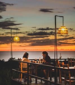 dos personas sentadas en una mesa con la puesta de sol en el fondo en Hotel Buenos Aires en Santa Teresa