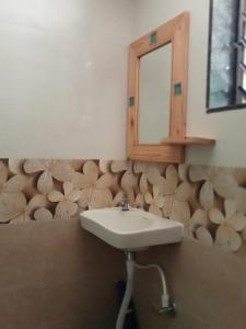 a bathroom with a sink and a mirror and wooden logs on the wall at Sai Homestay in Malvan